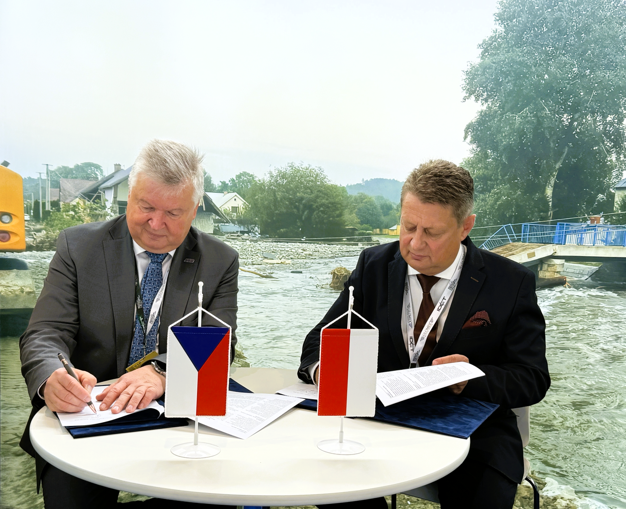 Mężczyźni przy stole podpisują porozumienie. Widać flagi polską i czeską